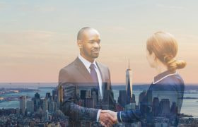 A businessman and businesswoman shaking hands with view of Manhattan in New York in the background.