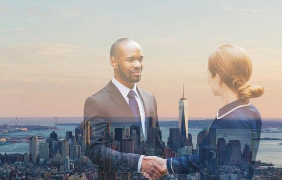 A businessman and businesswoman shaking hands with view of Manhattan in New York in the background.