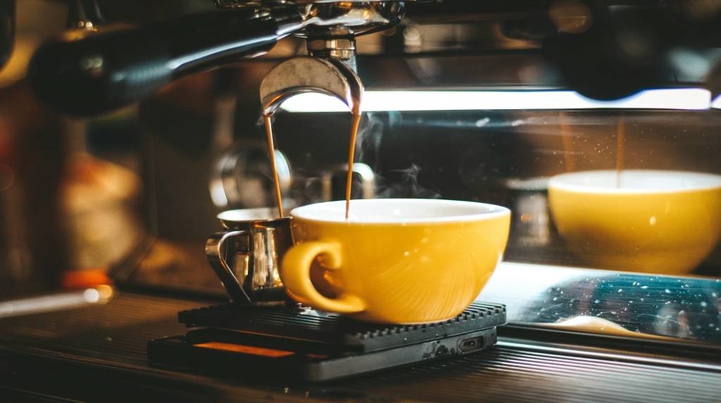 A close-up of an espresso machine pouring coffee into a yellow cup