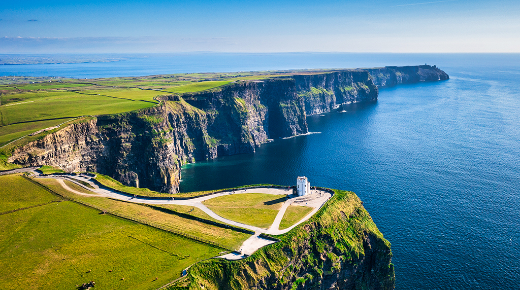 Aerial view of Ireland’s Cliffs of Moher with steep sea cliffs, green fields, and a small tower overlooking the Atlantic coastline.