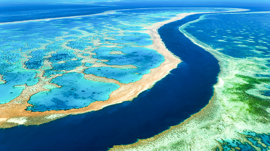 Aerial view of the Great Barrier Reef’s bright turquoise shallows and deep blue channel stretching across the seascape