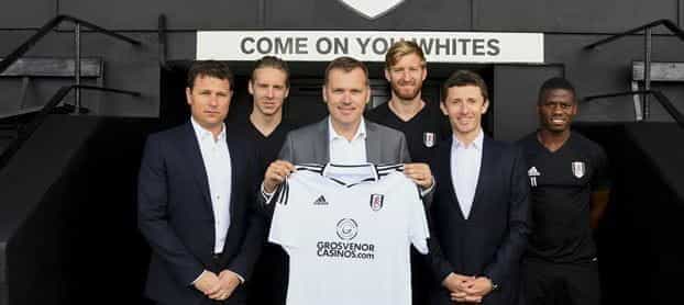 Fulham FC representatives hold up a home shirt with the new Grosvenor logo