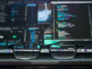 Glasses resting in front of a computer screen with lots of code and data.