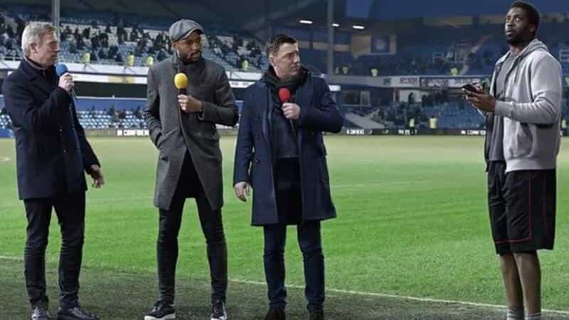 A man stands on a football field being interviewed by three other men.