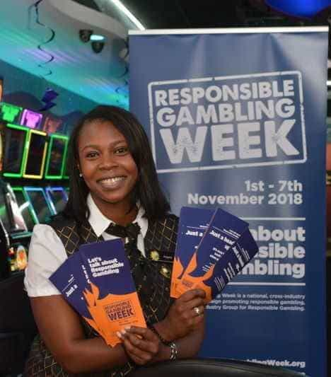 Woman holds leaflets in front of banner at Responsible Gambling Week event.