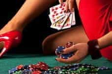A woman holding casino chips and cards, while placing her high-heeled foot on a casino table.