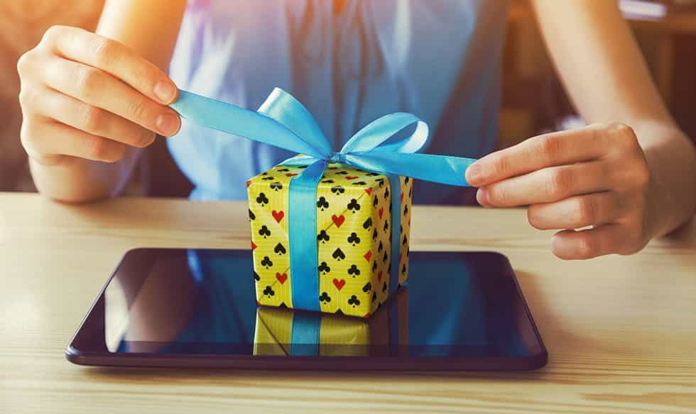 A woman unwrapping a gift that is wrapped in playing cards paper, and sitting on top of a tablet device.