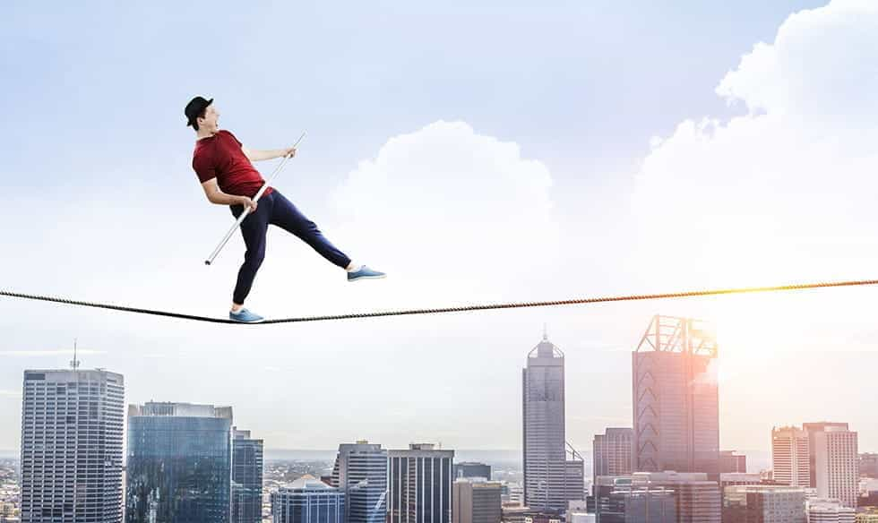 A man walking across a tightrope, over a cityscape.