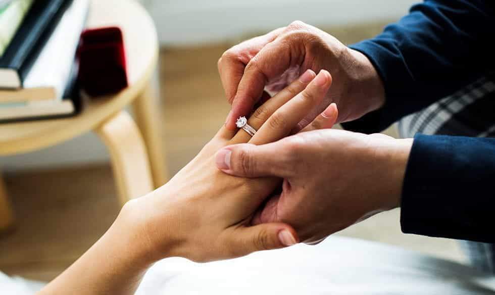 A man putting an engagement ring on a woman's finger.