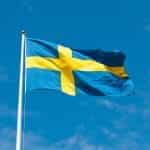 The Swedish flag flutters in the breeze against a clear blue sky..