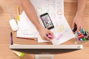 Person drawing on papers next to a smartphone.