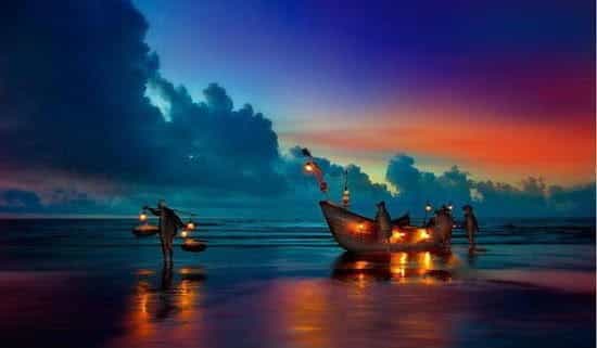 Sunset at the beach at Cox’s Bazar. A boat lit by lanterns docks at the shore.