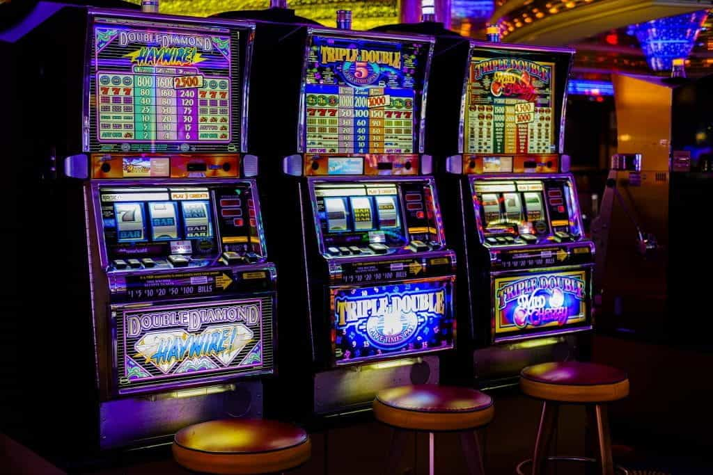 Image of three colorful and brightly lit slot machines in an arcade.