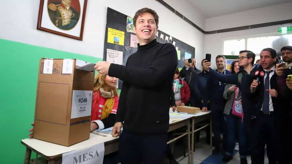 Axel Kiciloff smiles as he casts a vote, surrounded by photographers and journalists.