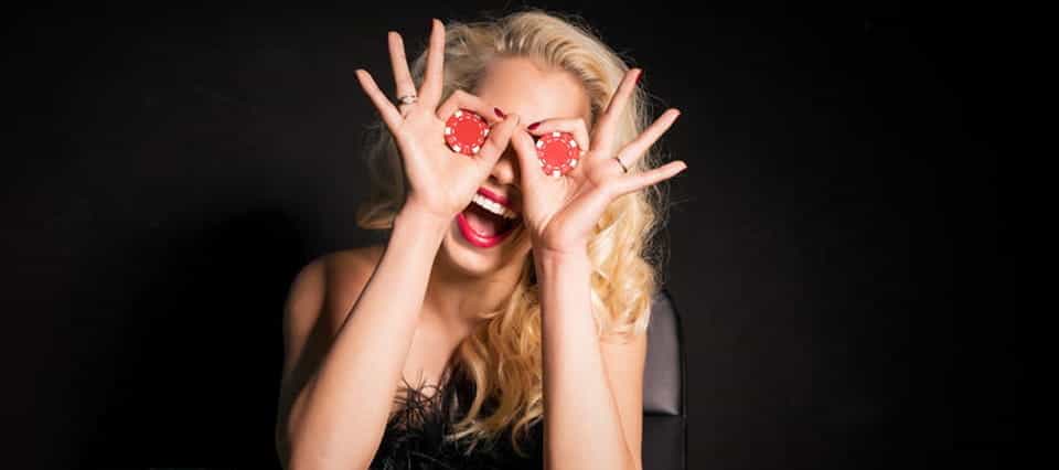 A woman holds casino chips over her eyes and smiles widely.