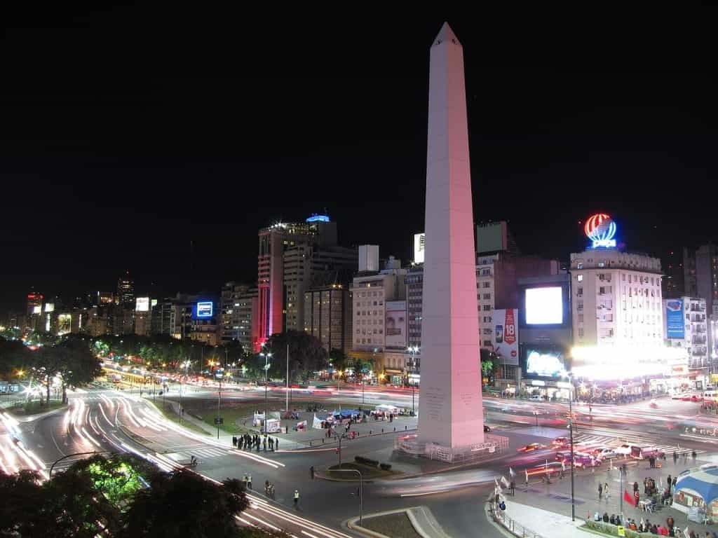 A view of the Buenos Aires obelisk, surrounded by traffic, at night.
