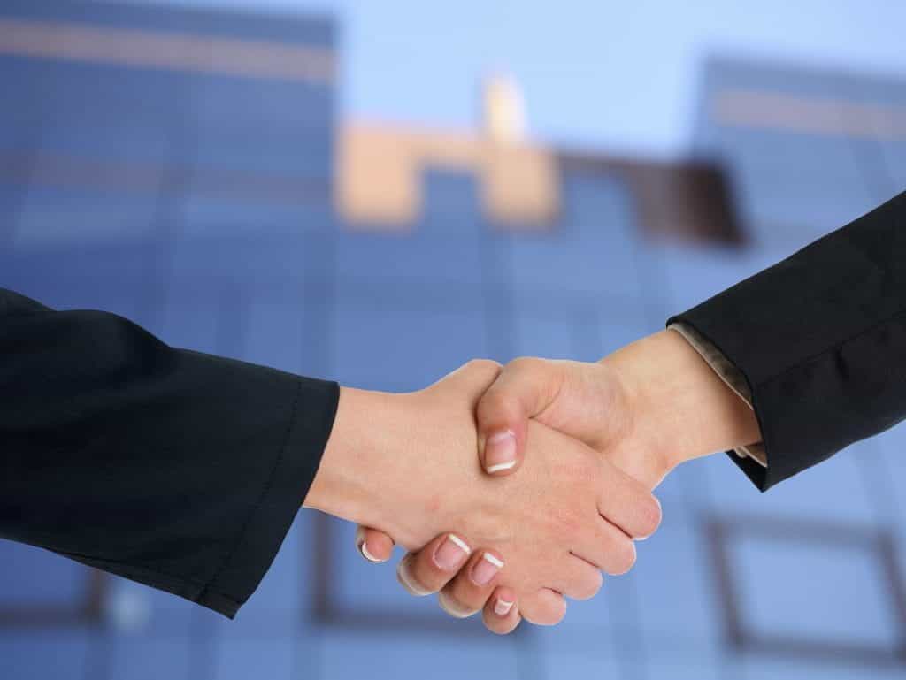 A closeup of a handshake between two white hands wearing suit jackets. 