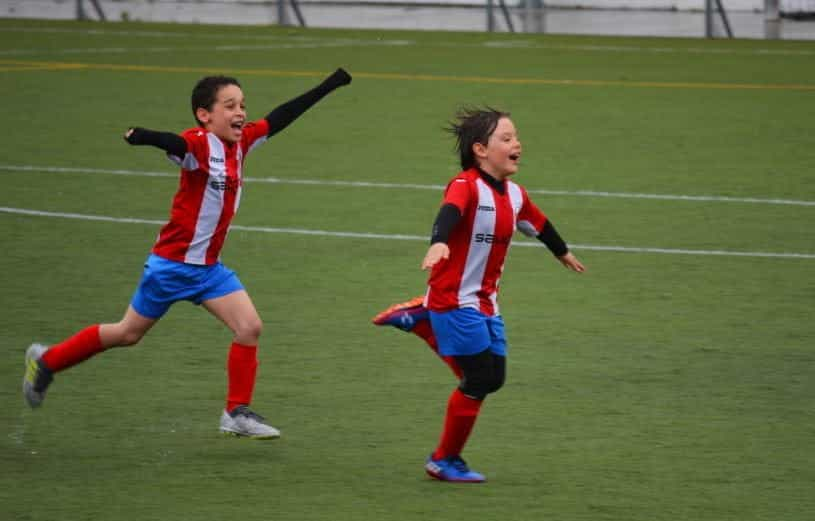 Two young children play football together on a pitch. 