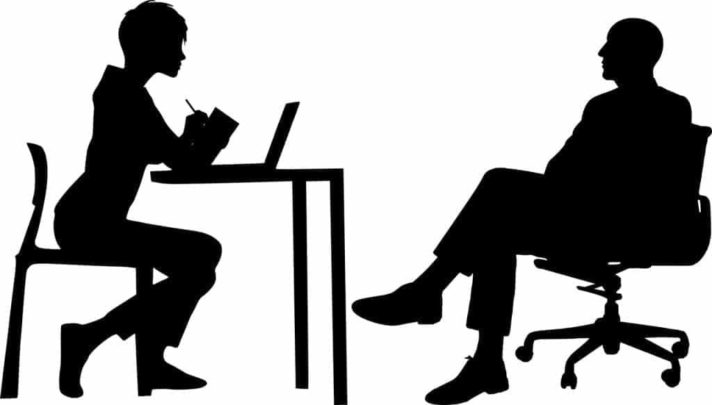 Black and white silhouettes of figures on either side of a desk, discussing.