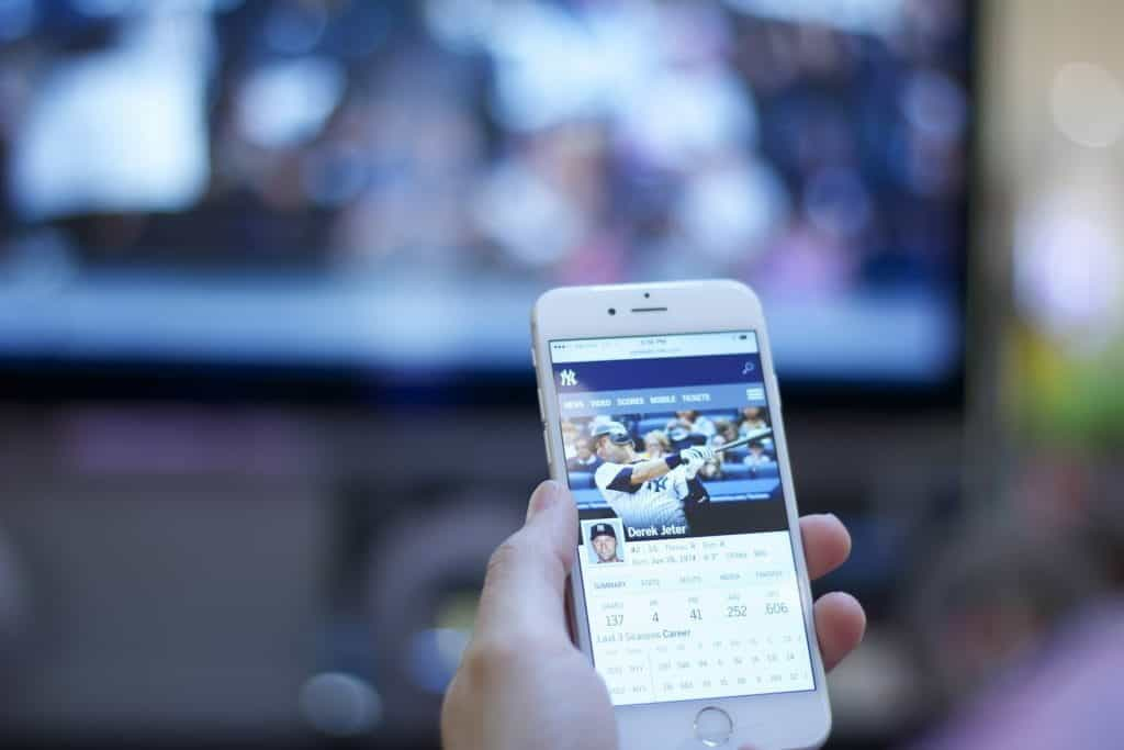 A hand holds up an iPhone and looks at baseball stats.