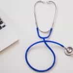 A blue stethoscope next to a laptop on a white background.