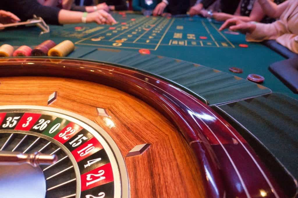 A roulette wheel sits still while gamblers sit at the opposite end of the table.