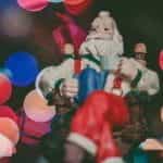 A festive Santa Claus figurine in front of twinkling Christmas lights.
