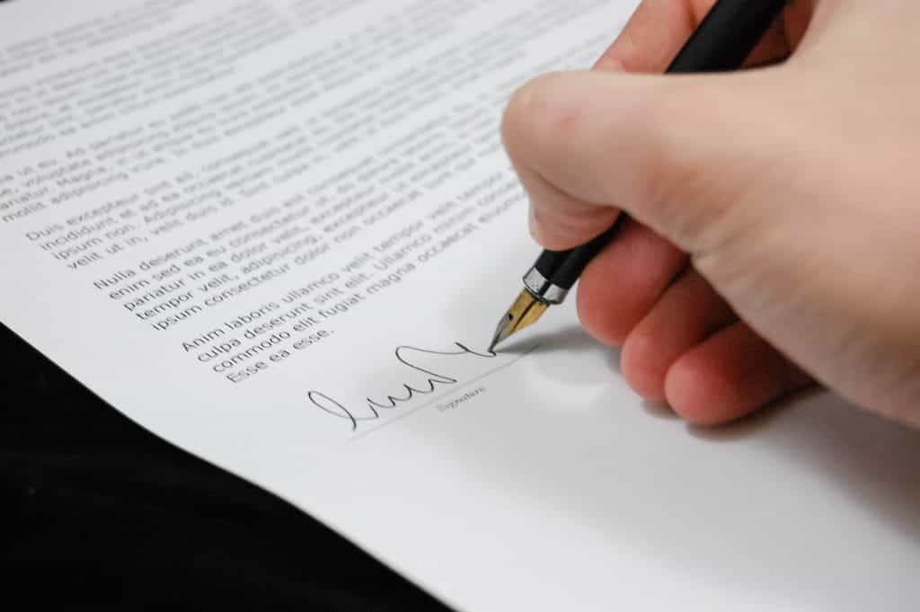 A white hand signs at the bottom of a contract.