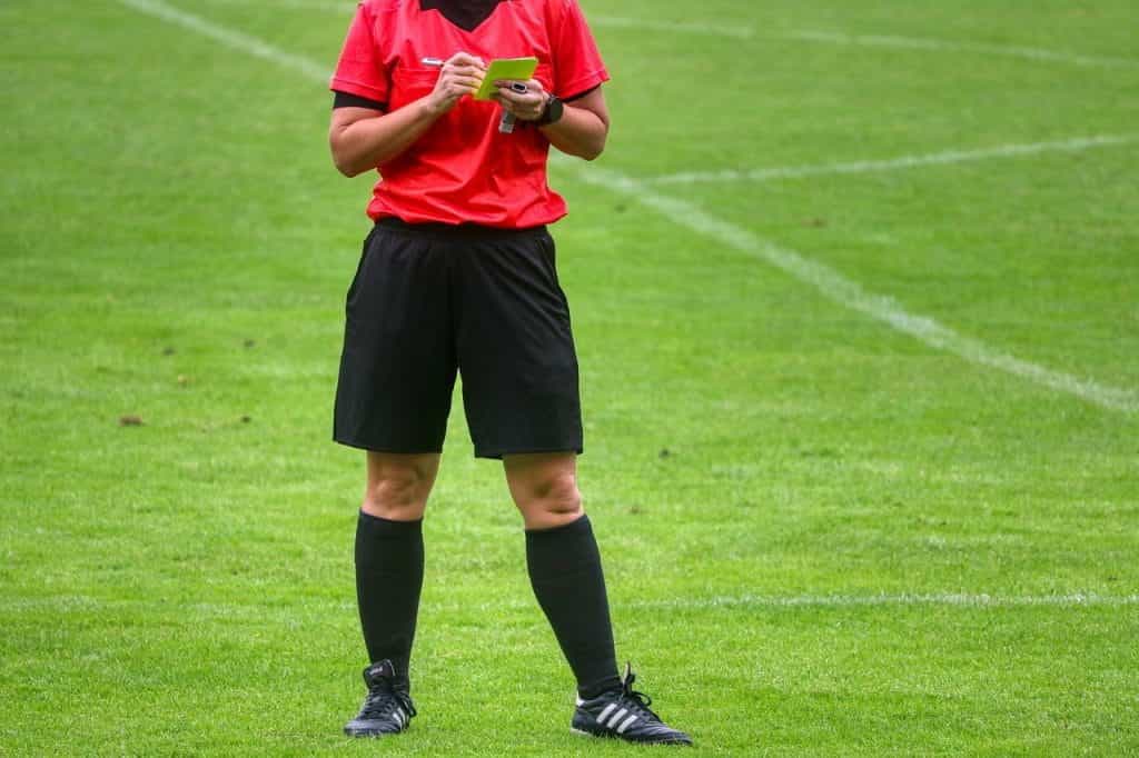 A referee holding a yellow card on football pitch.