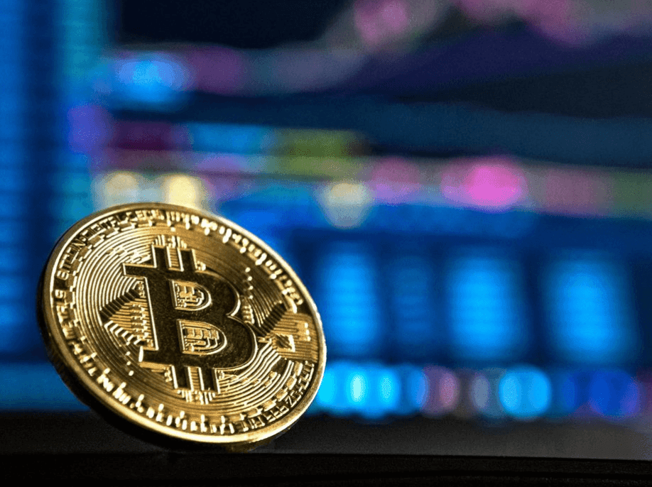 A color photograph of a gold Bitcoin in front of a blurry blue background.