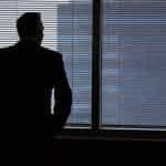 A silhouette of a business man looking out of a window.