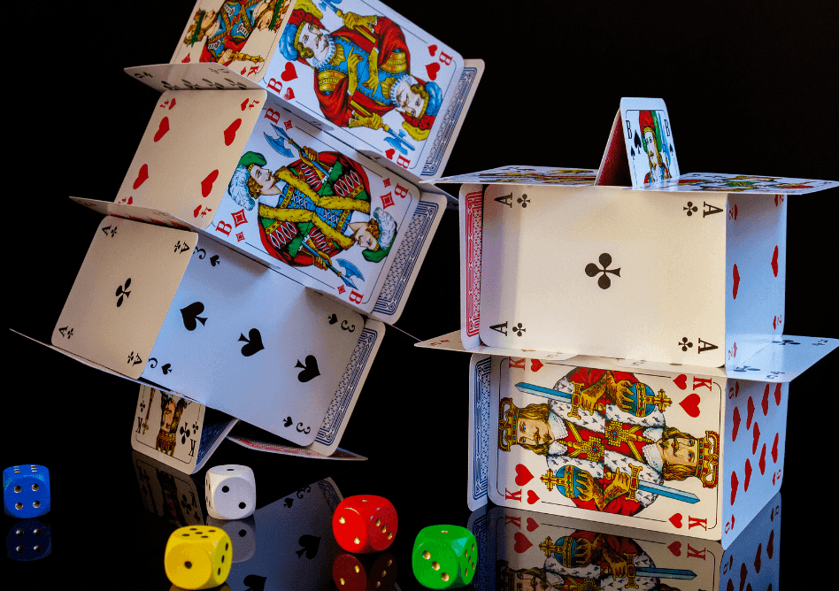Two houses of cards stand behind a number of colorful dice.