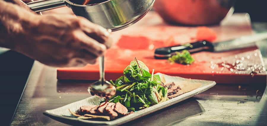 A chef drizzling sauce over a plate of duck and salad.