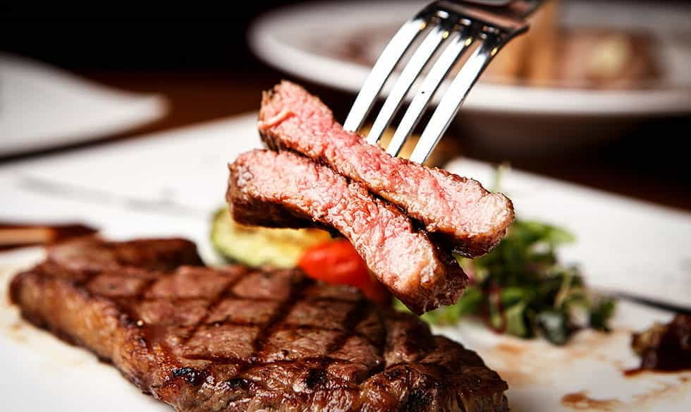 A plate with steak, with a fork holding two slices of meat in the air.