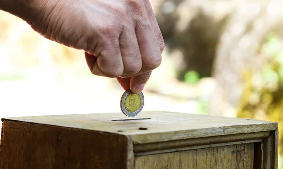 A hand placing a coin in a charity box.