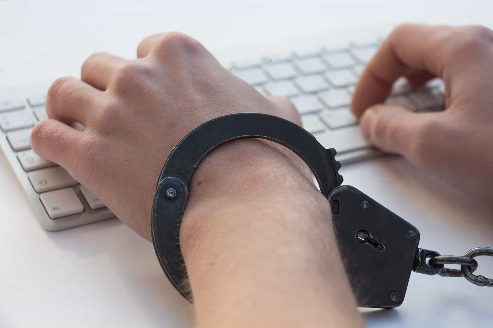 A set of white hands are handcuffed to a Mac computer keypad.