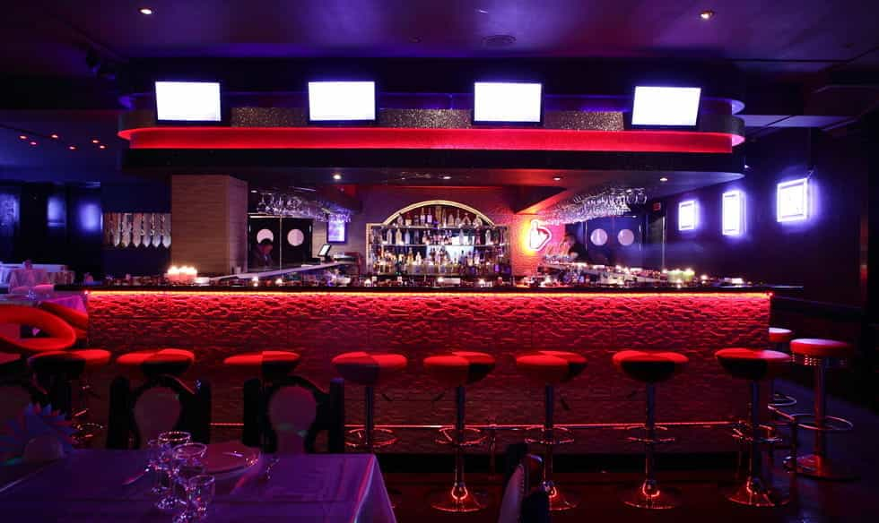 A fancy bar with red decor and purple lighting.