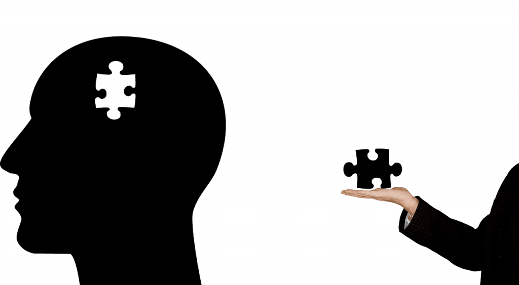 A silhouette of a head with a jigsaw-shaped hole in it. Another person is holding the missing piece.