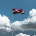 The Latvian flag flying from a flagpole with the sky in the background.