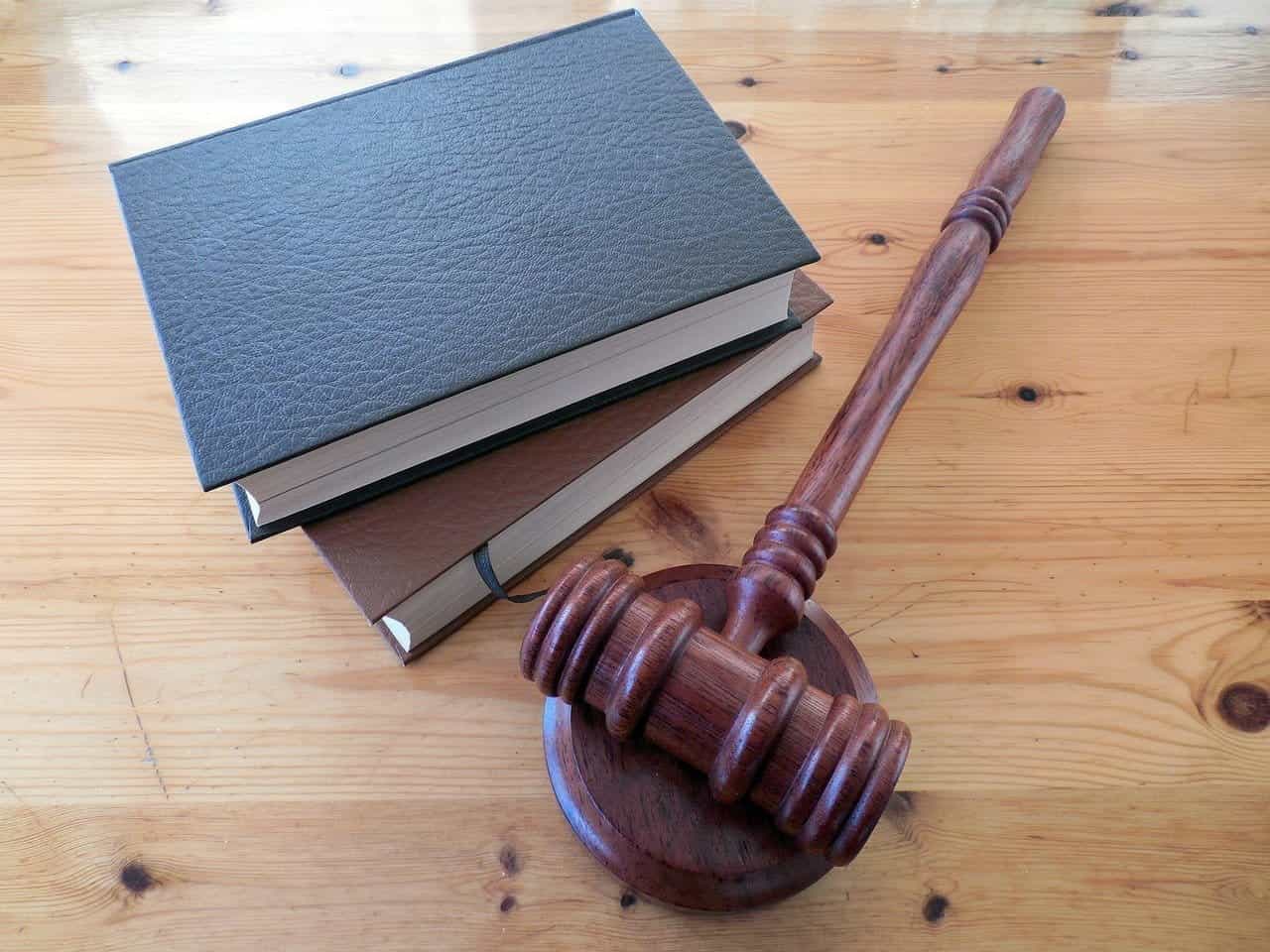A stack of legal books sits behind a gavel on a desk.