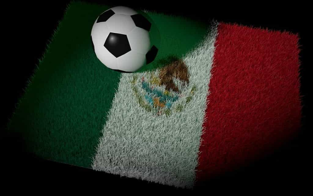 A soccer ball sits on a patch of grass illuminated in the design of Mexico’s flag.