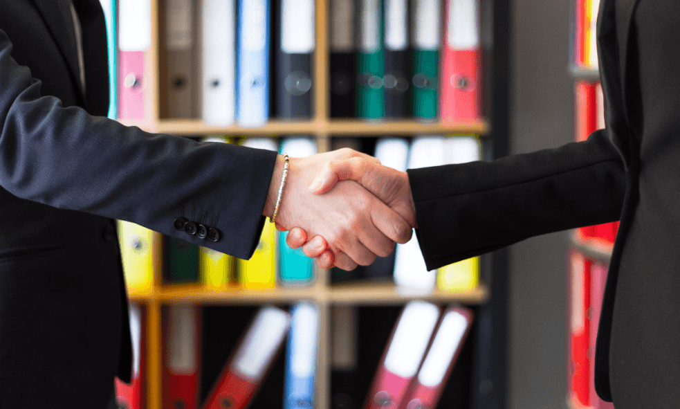 Two business partners shake hands on a deal, in an office.