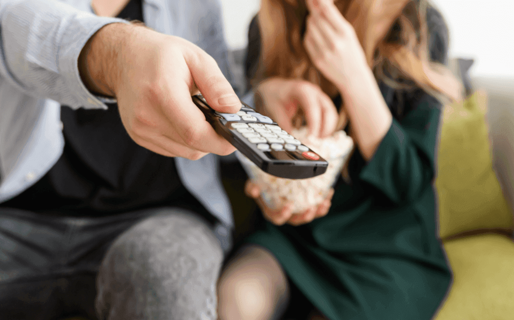 Man pointing a remote at the tv and woman eating popcorn.
