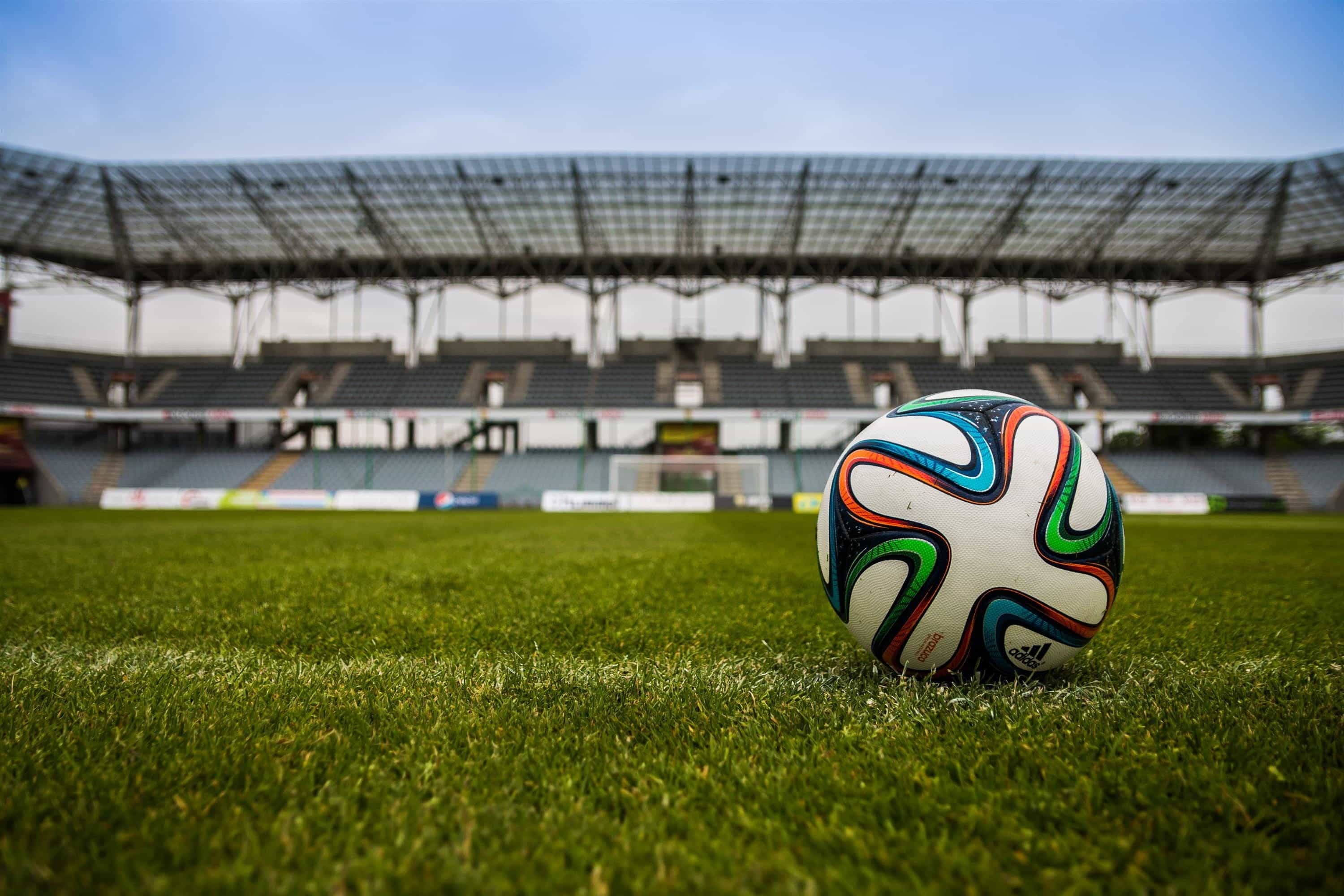 A football in the foreground of an empty stadium.