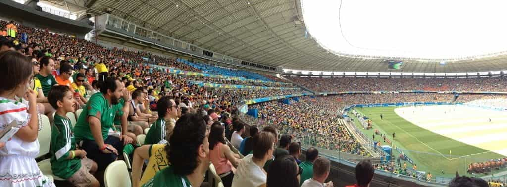 Soccer fans, many of whom wearing Mexico team jerseys, eagerly watch an ongoing soccer game at a stadium in the day.