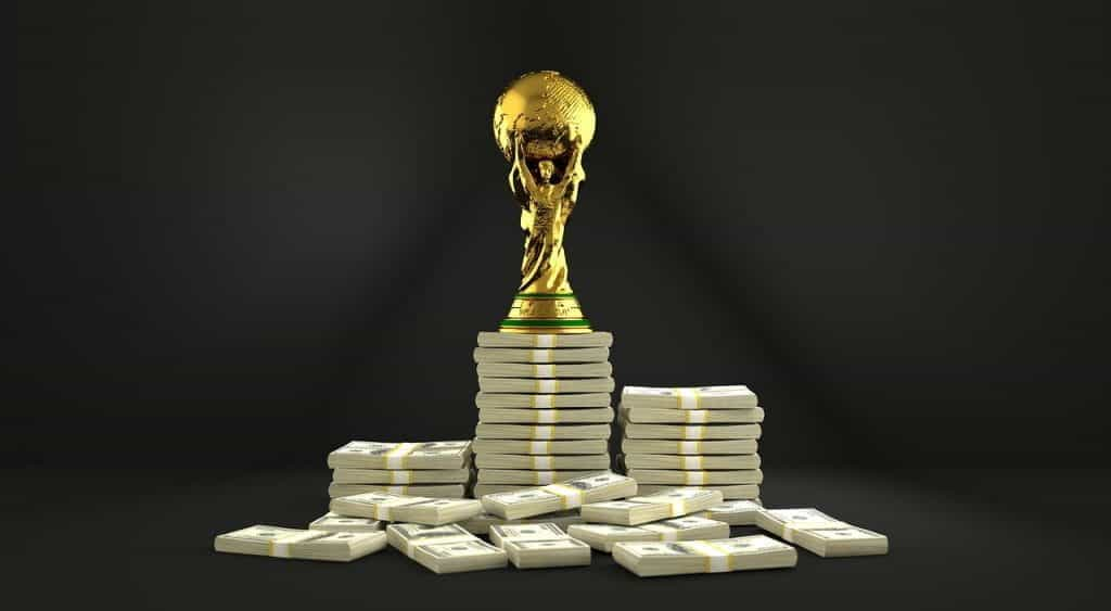 An image of a golden soccer trophy atop a large pile of money.