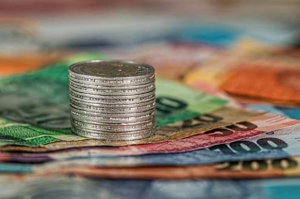 A stack of coins on top of some bank notes.