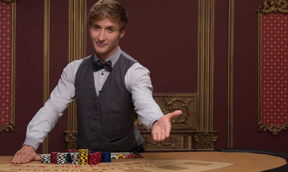 A casino croupier, offering a seat at his gaming table.
