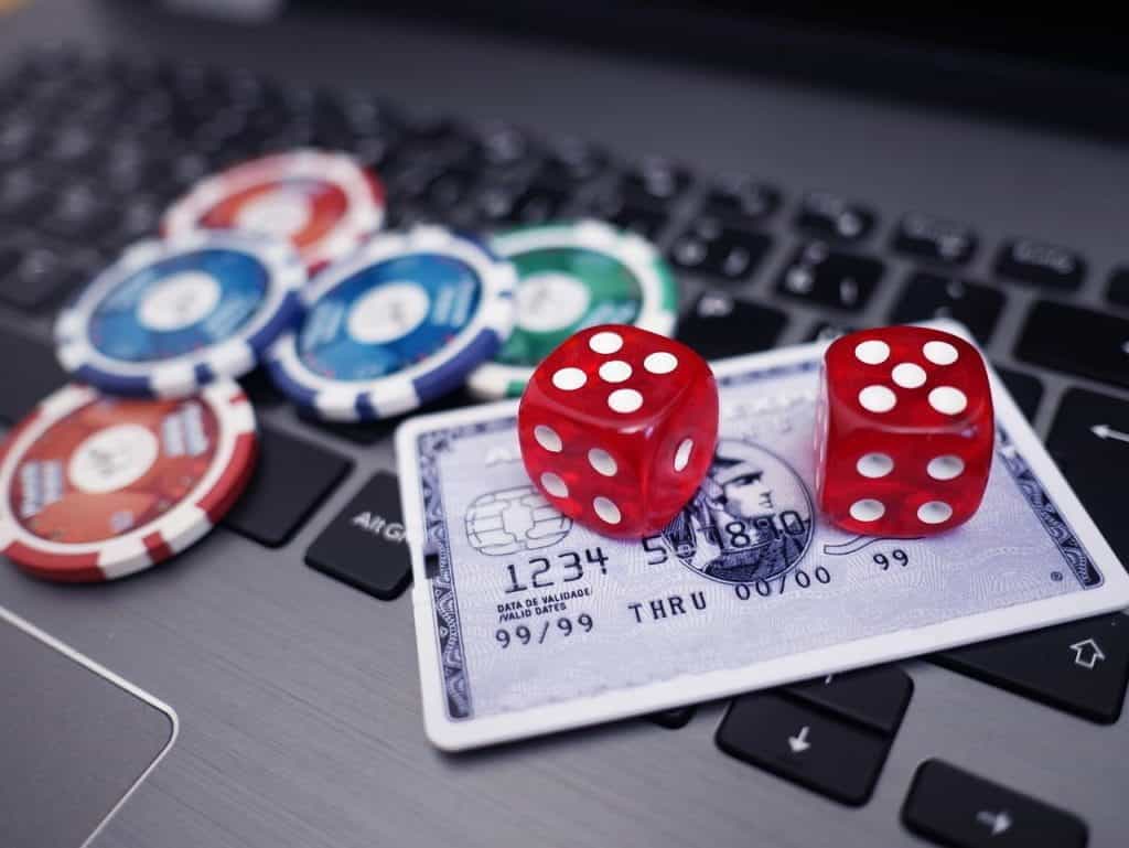 A computer keyboard with poker chips, red dice, and a credit card laying on top to indicate online gambling.