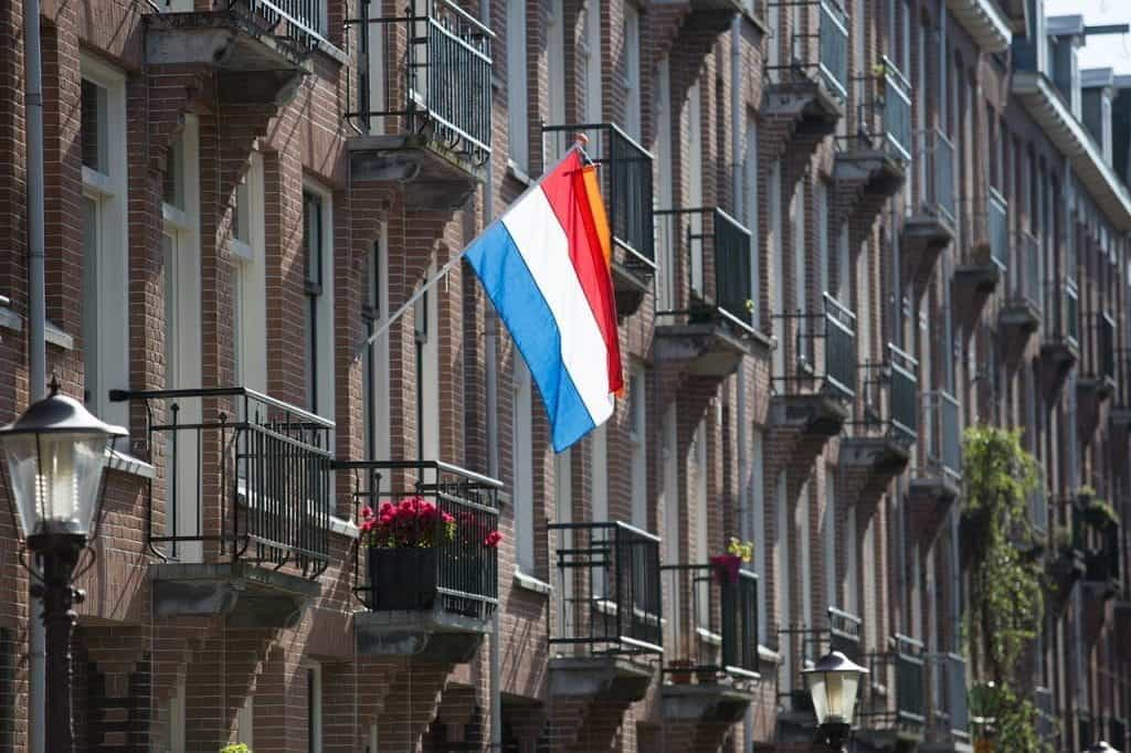 The Dutch flag hanging from a flag pole on a building.